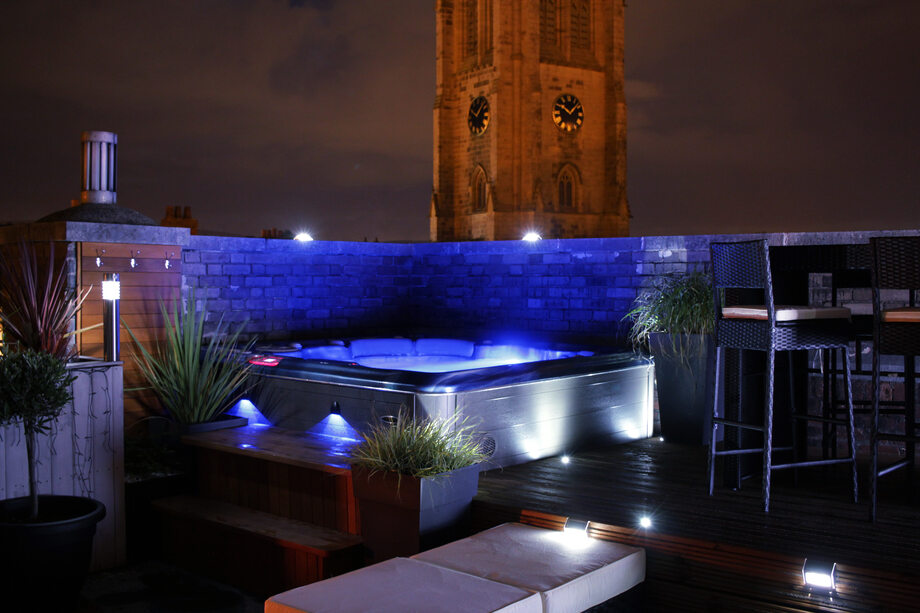 Un spa est installé sur une terrasse. Son eau est éclairée par des lumières (chromothérapie).