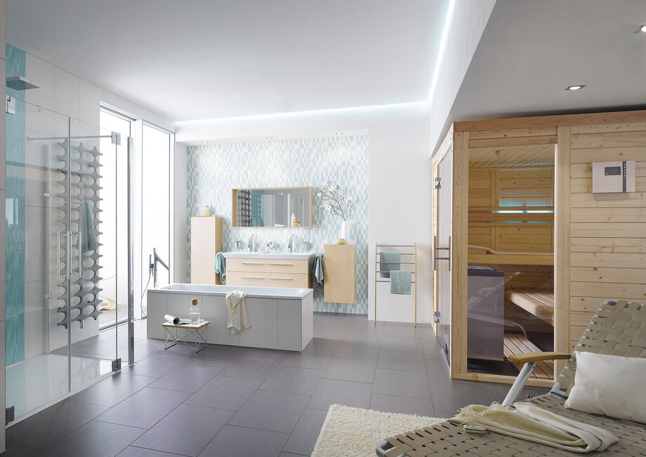 Un sauna est installé dans l'angle d'une grande salle de bain, à proximité d'une douche et d'une baignoire. 