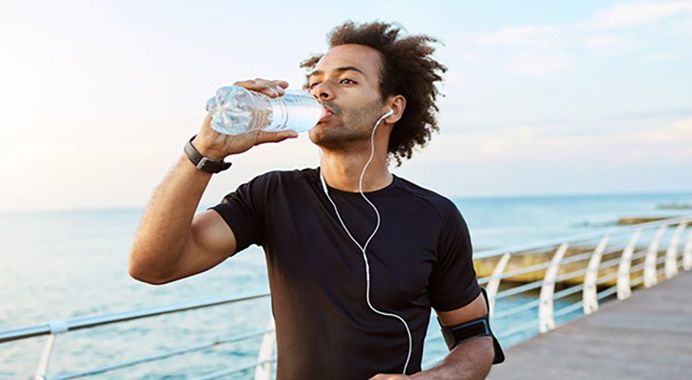 Un homme, lors d'une séance de sport, boit de l'eau. L'hydratation et l'activité physique font partie des façons de diminuer l'inflammation dans le corps naturellement.