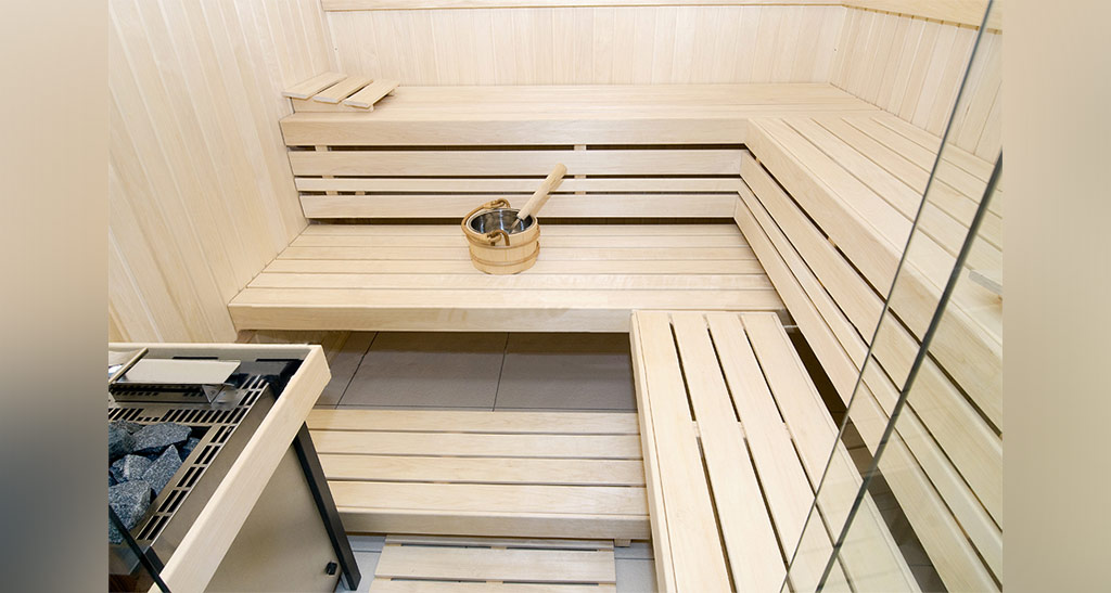 Zoom sur l'intérieur d'un sauna Lambris Design avec deux rangées d'assises un seau et un four.