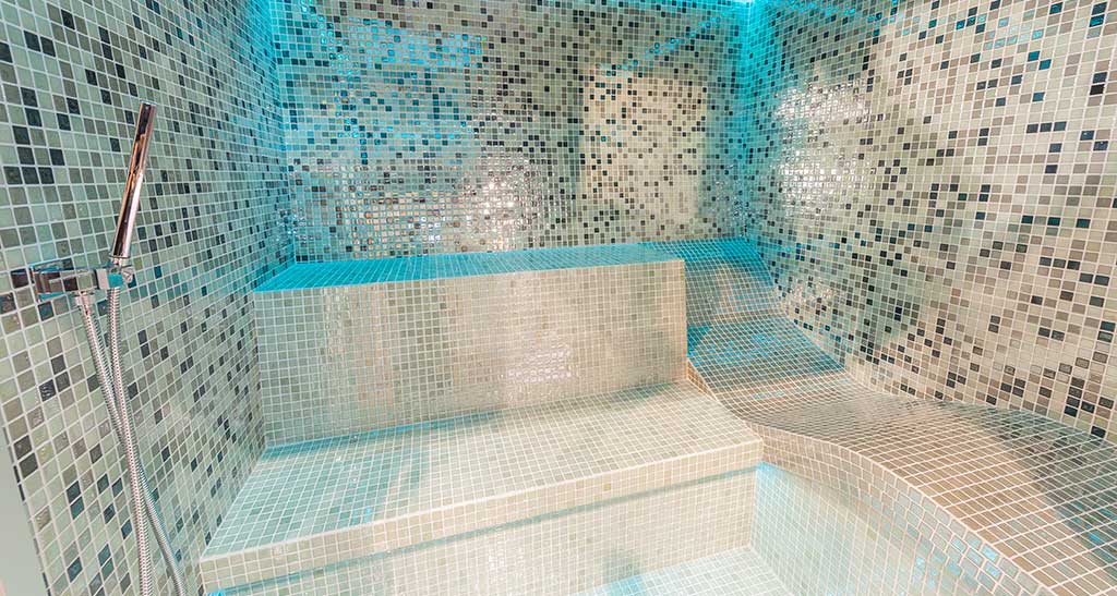 Hammam Ovation Lounge avec places assises et une place allongée et une lumière d'ambiance bleu.