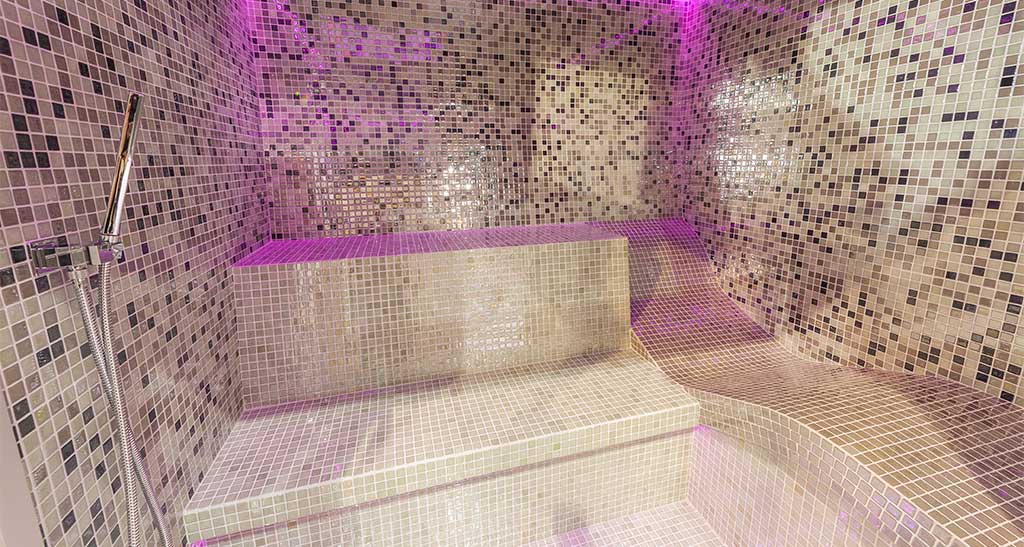 Hammam Ovation Lounge avec places assises et une place allongée et une lumière d'ambiance rose.