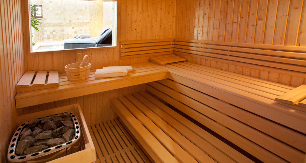 Intérieur d'un sauna Lambris Sensation avec un seau, un four, deux serviettes le tout donnant sur une chaise longue dans une pièce.