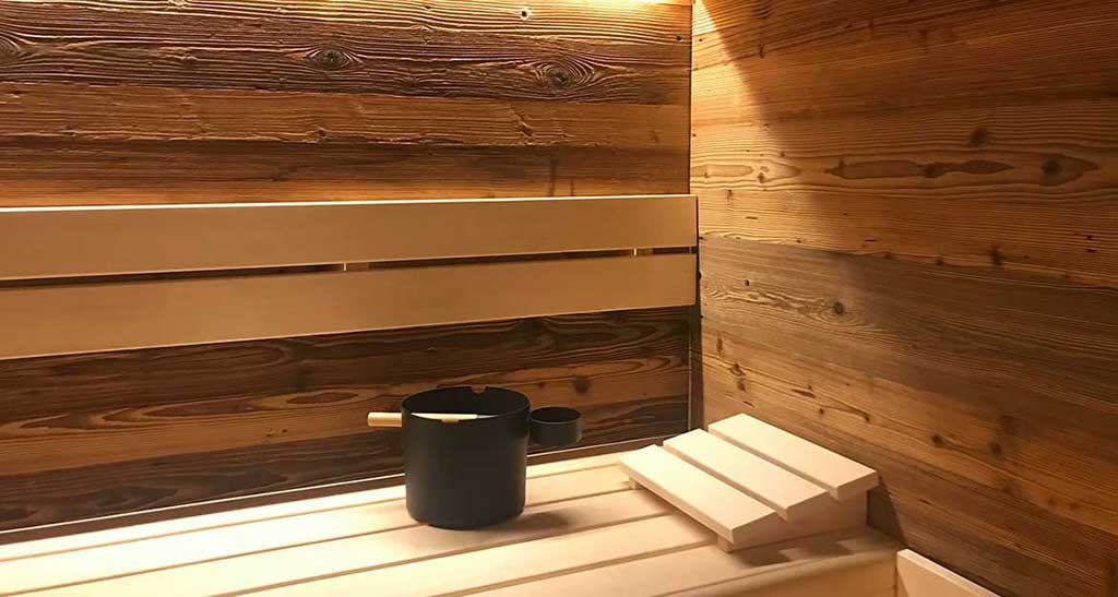 Zoom sur une seau posé sur l'assise d'un sauna Lambris Design Plus avec une lumière d'ambiance tamisée.