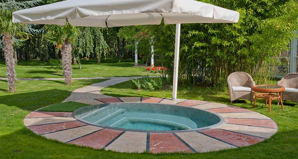 Spa mosaïque Ellipse dans un jardin avec un parasol au dessus.