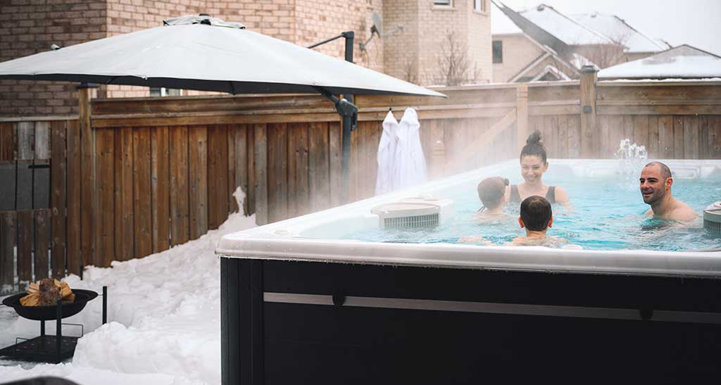 Spa de nage 17AX posé dans un jardin enneigé avec une famille qui se baigne.