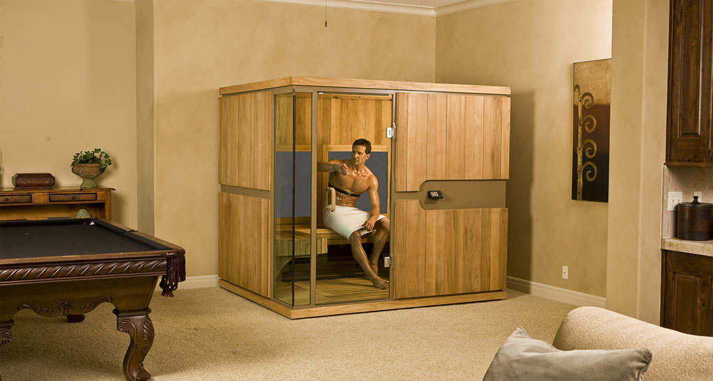Homme en serviette qui regarde son poignet avec un moniteur cardiaque autour de la poitrine dans une cabine sauna Infrarouge Grand Confort dans une salle avec une table de billard à côté.