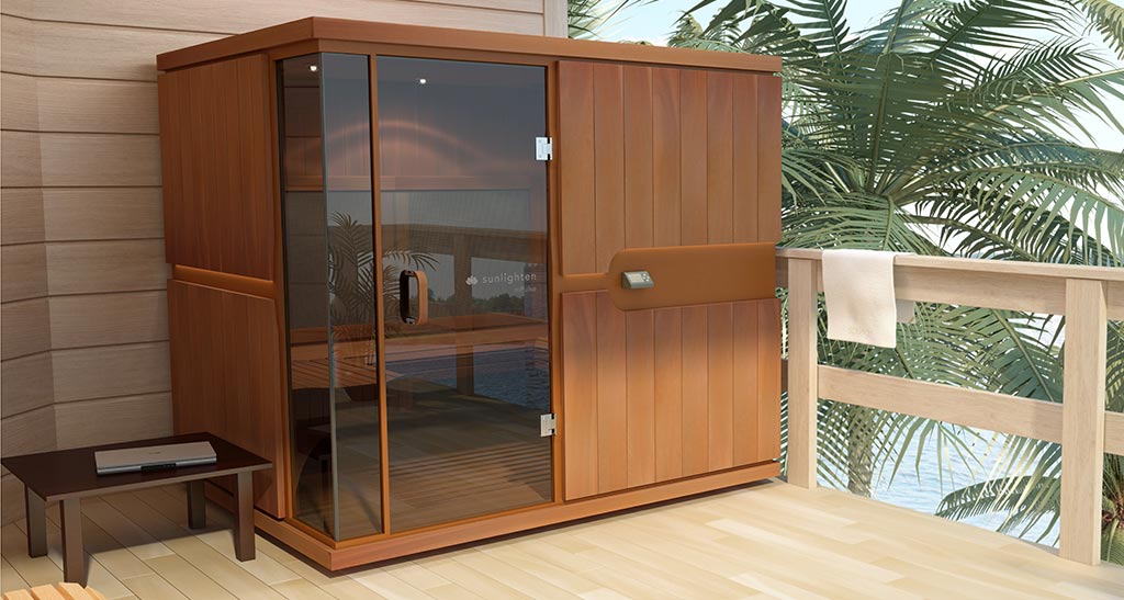 Cabine sauna Infrarouge Grand Confort sur une terrasse en bois avec un palmier d'un côté et une table basse avec un ordinateur de l'autre côté.