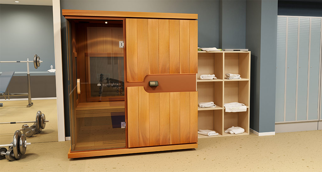 Cabine sauna infrarouge Trio dans une salle de sport avec une étagère de serviettes d'un côté et des haltères de l'autre.