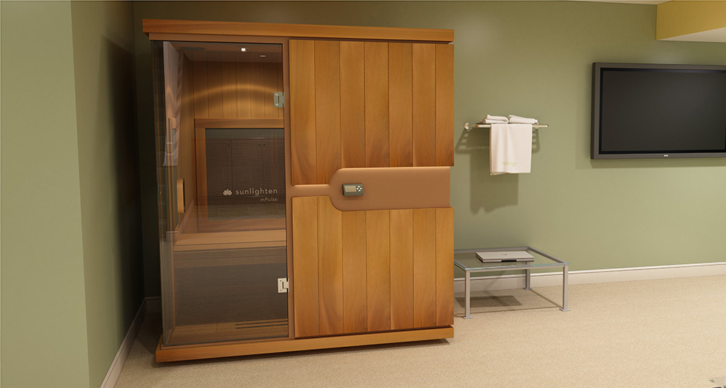 Cabine sauna Infrarouge Trio avec portes vitrées dans une pièce avec un séchoir avec serviettes étendue et une table de chevet avec un ordinateur et une télévision sur le côté.
