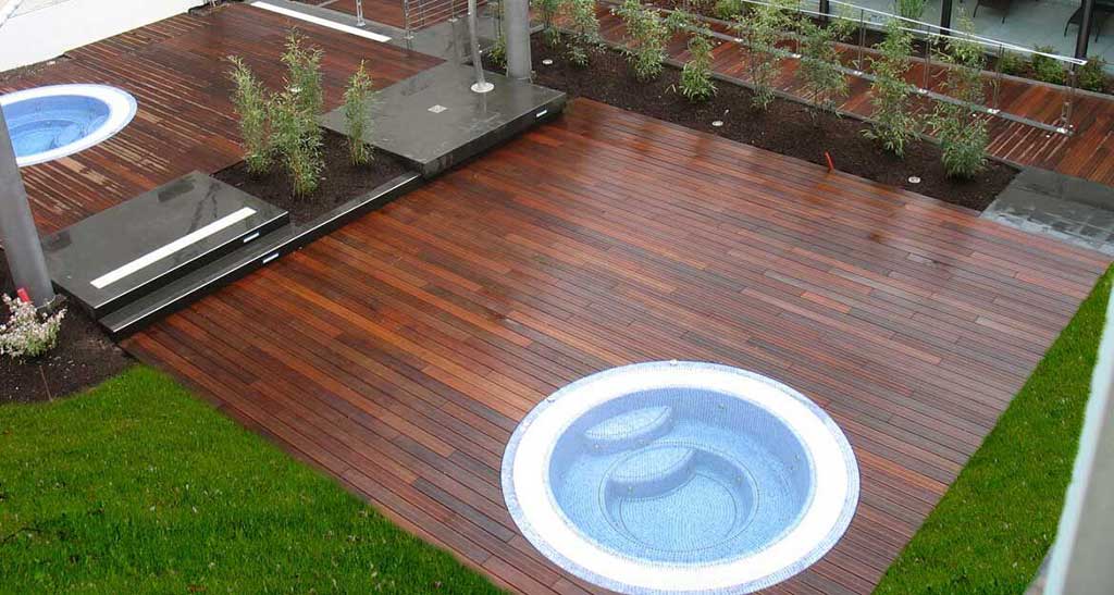 Spa à débordement Mosaic 300 encastré dans une terrasse en bois entourée de plantes