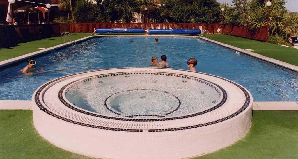 Spa à débordement Mosaic 300 semi encastré à côté d'une piscine avec des enfants dedans.
