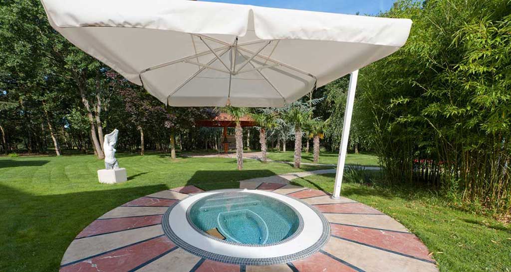 Spa à débordement Mosaic 360 encastré dans un jardin plein de verdure sous un parasol.