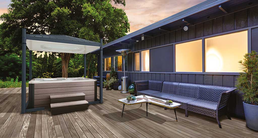Abri Hydrocover pour spa ouvert sur une terrasse aménagée avec un coin salon de jardin à l'arrière d'une maison illuminée