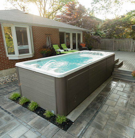 Spa de nage portable installé sur une terrasse en carrelage avec des plantes devant