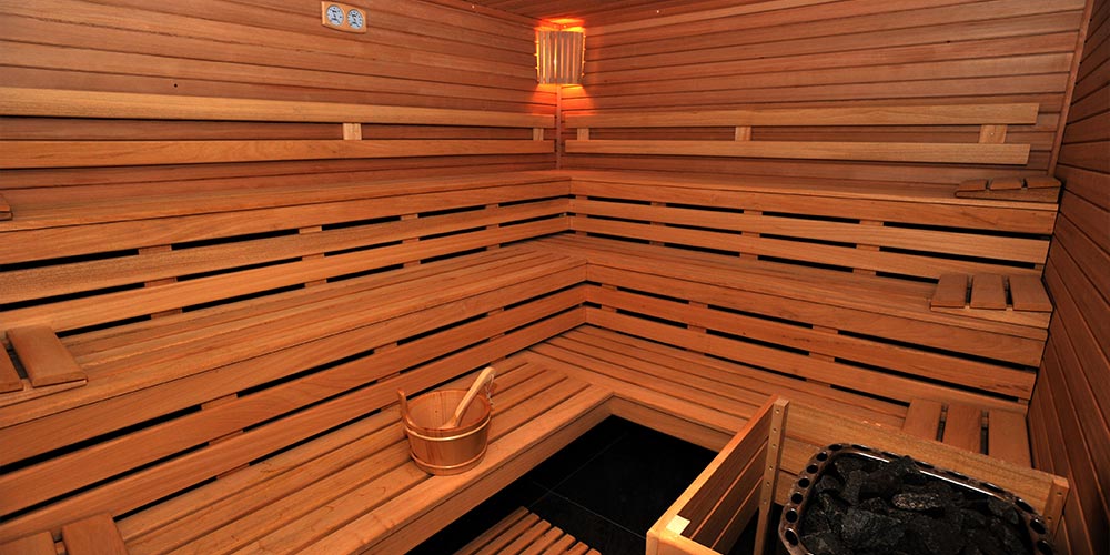 Sauna en bois avec plusieurs banquette, un seau et une louche