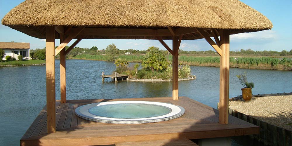 Spa mosaïque encastré dans une terrasse en bois avec une tonnelle au-dessus et un étang à côté