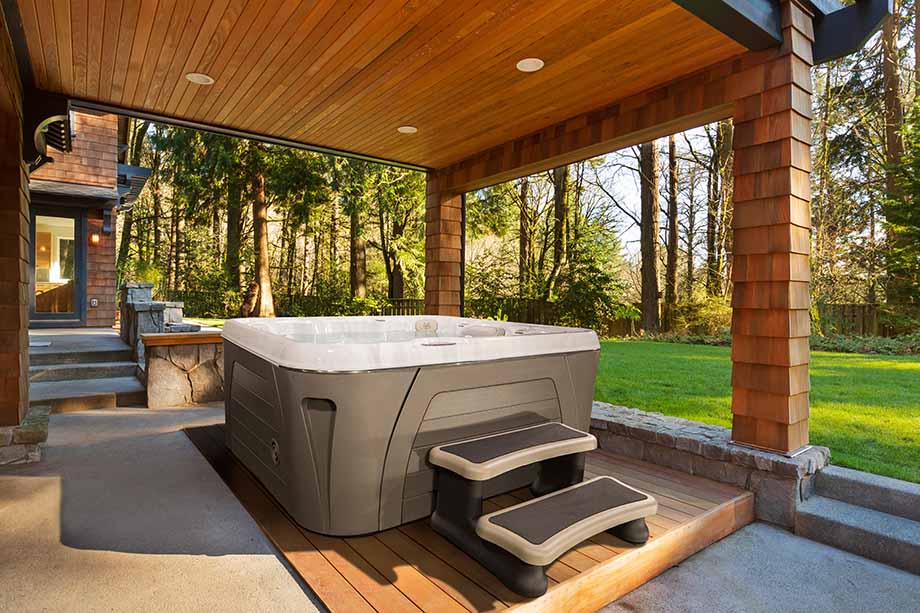 Un spa portable donne sur un jardin. Il est installé sur une terrasse, sous un abri en bois. 