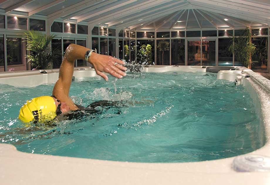 Une personne pratique la natation dans un spa de nage installé en intérieur