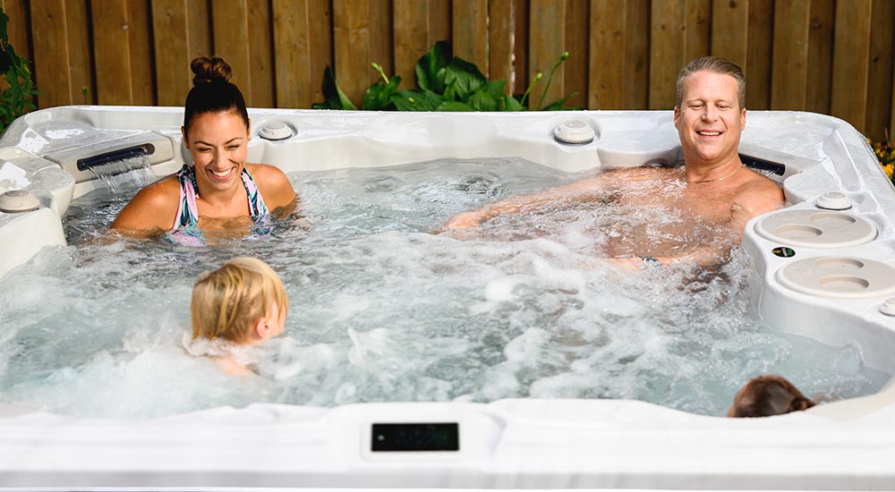 Parents et enfants partagent un moment de convivialité dans un spa installé en extérieur et utilisent les jets de massage.