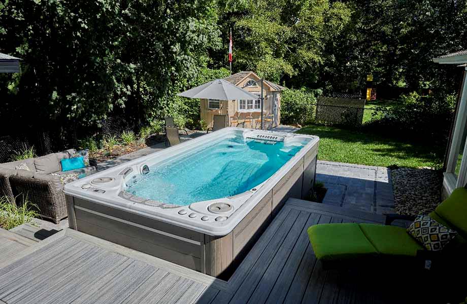 Un spa de nage est encastré dans une terrasse en bois et offre une vue sur le jardin. 