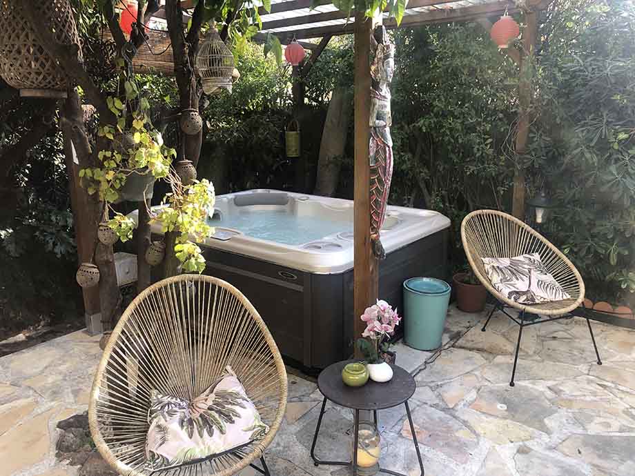 Un spa portable est installé en extérieur sur une terrasse. Deux chaises confortables sont placés à côté du bain à remous. Une décoration inspirée de la culture asiatique entoure le spa.  