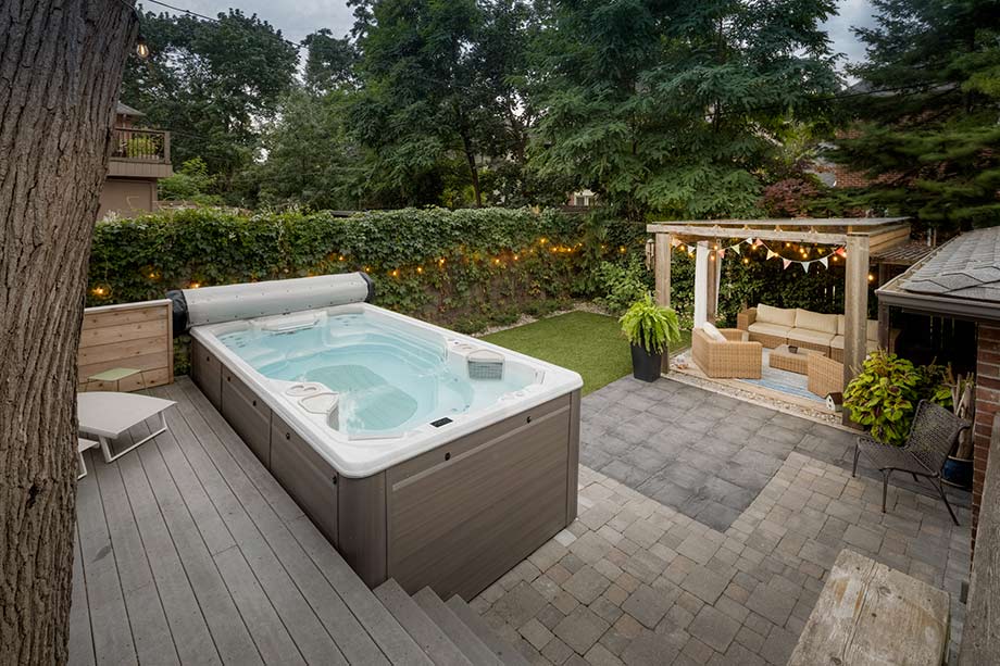 Un spa de nage portable (ou hors sol) est placé sur une terrasse, à proximité d'un salon de jardin. 