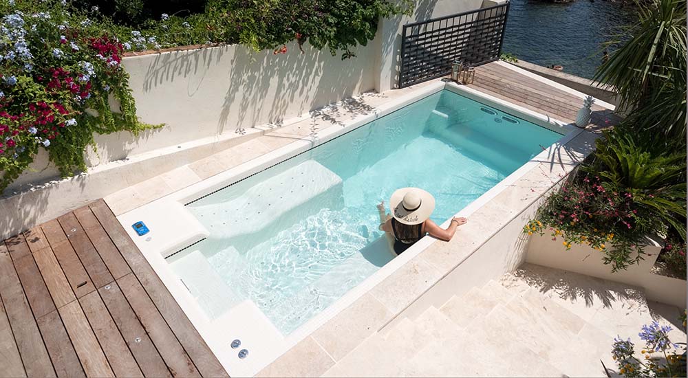 Spa de nage ou couloir de nage : comment choisir ? Sur cette photo, une femme est installée sur une assise d'un spa de nage encastré dans une terrasse.