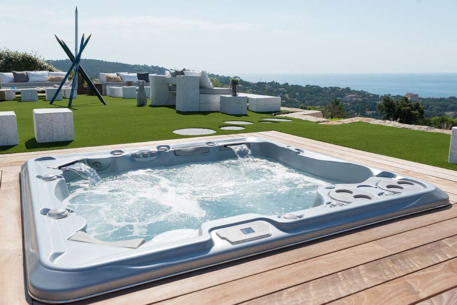 Un spa est encastré dans une terrasse, dans un jardin offrant une vue sur la mer. 