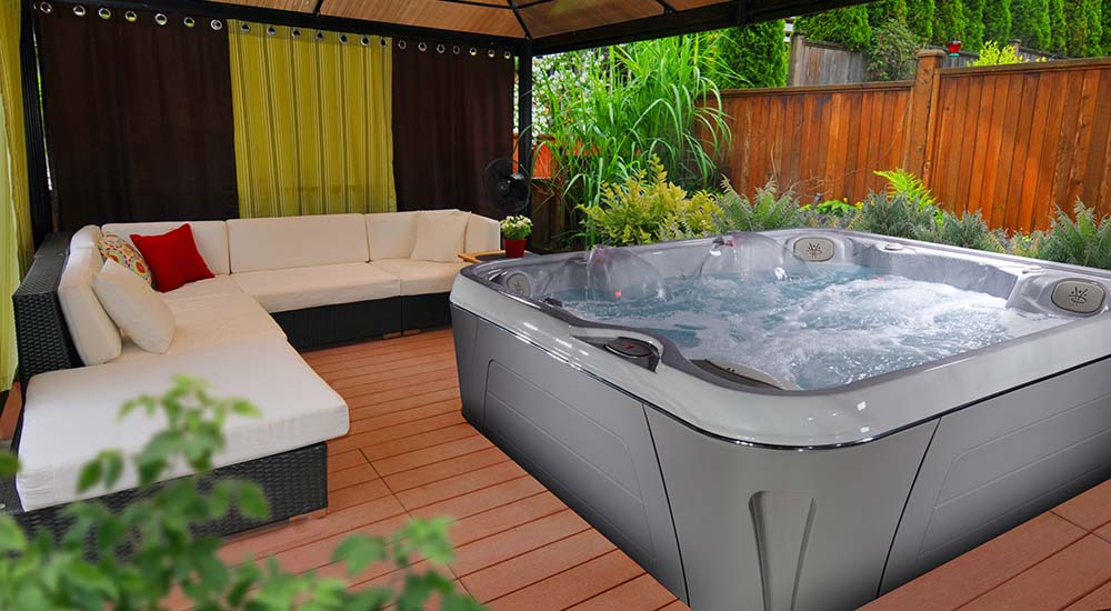 Quelle est la consommation d'eau d'un spa ? Un spa portable est placé sur une terrasse en bois, à proximité d'un salon de jardin et sous un abri.
