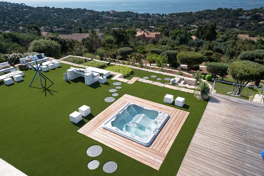 Un spa avec deux places allongées est encastré dans une terrasse, au coeur d'un jardin contemporain. 