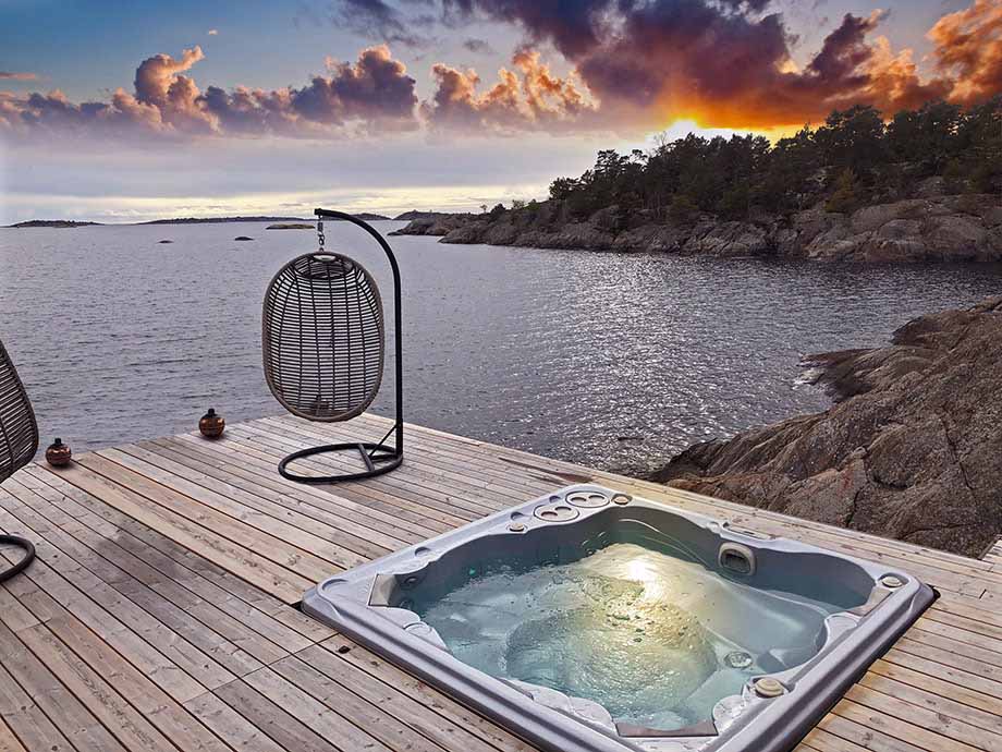 Un spa avec une place allongée est installé sur une terrasse en bois. Il offre une vue magnifique sur la mer et un coucher de soleil. 