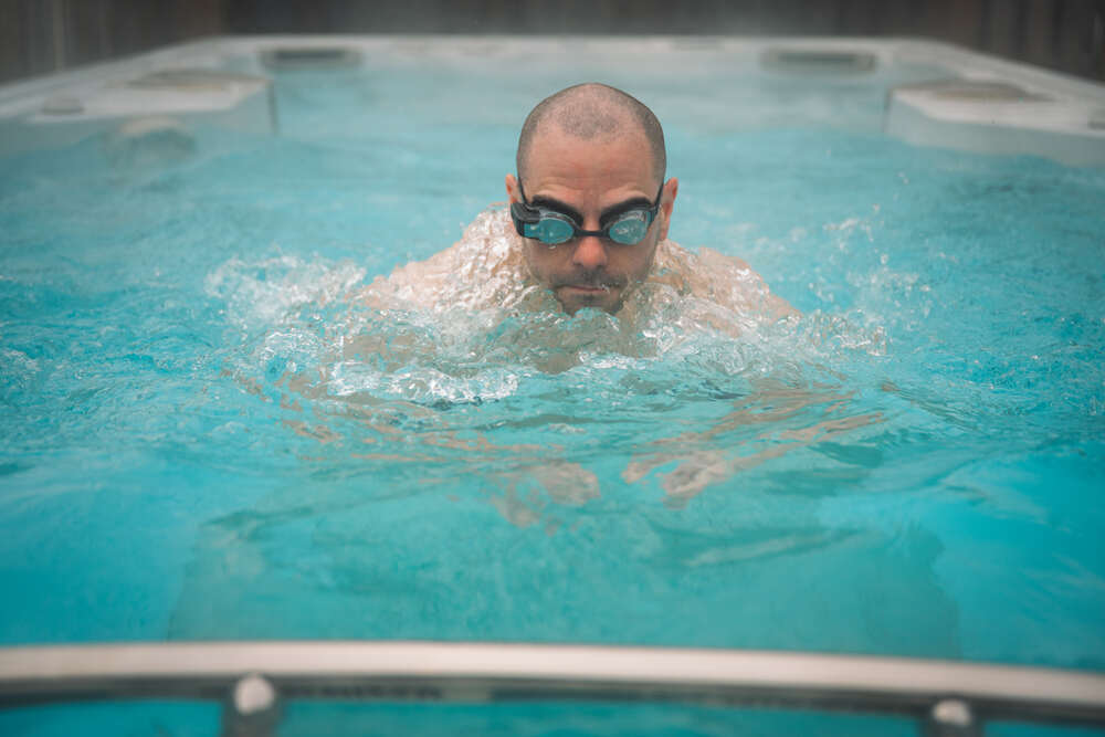 Un homme, équipé de lunettes de natation, nage la brasse dans un spa de nage et lutte contre le contre-courant. 