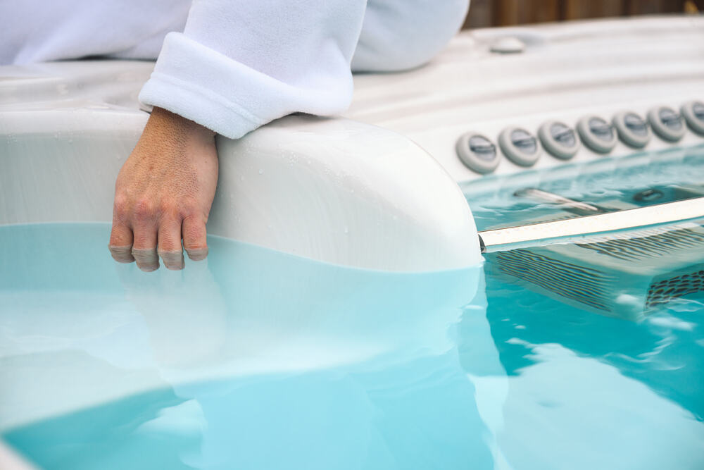 Un homme plonge sa main dans un spa de nage pour vérifier la température de l'eau. 