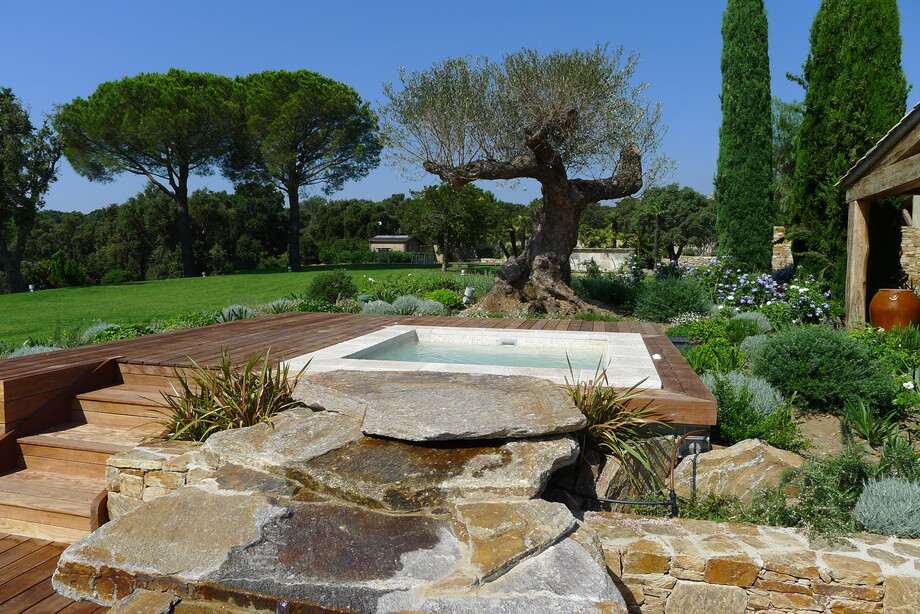 Un spa carré en mosaïque est implanté dans un jardin paysager. 