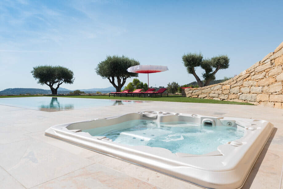 Un spa encastré est intégré dans une terrasse juste à côté d'une piscine à débordement. 