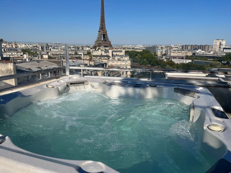 Un spa portable est installé sur une terrasse. Les utilisateurs profitent d'une vue sur les toits de Paris et la tour Eiffel. 