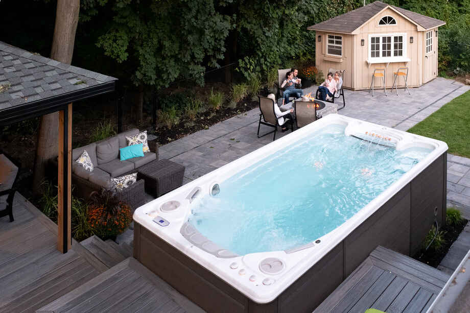 Pour déterminer la taille de spa de nage idéale, il faut prendre en compte l'espace d'installation disponible. Ici, un spa de nage est installé sur une terrasse dans un jardin.