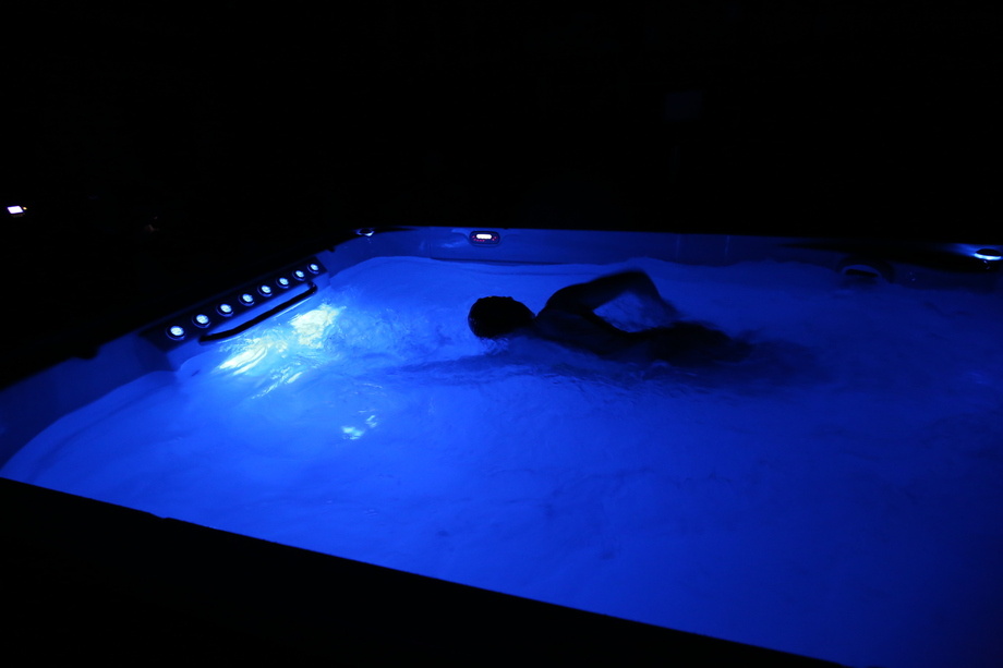 Un homme nage dans un spa de nage en pleine nuit. Le bassin dispose d'un éclairage. 