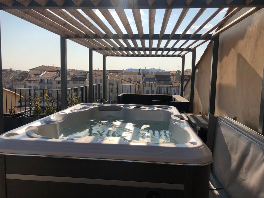 Un spa portable est installé sur une terrasse et bénéficie d'une vue sur les toits d'une ville. 