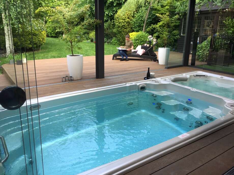 Un spa de nage est installé dans une véranda ouverte et bénéficie d'une vue sur le jardin. 
