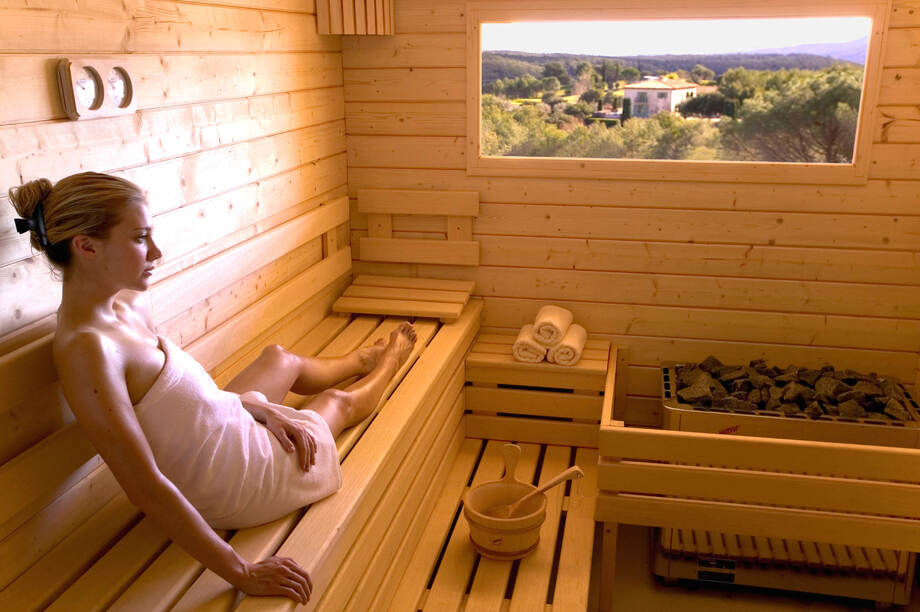 Une femme est installée dans un sauna traditionnel qui dispose d'une fenêtre avec une vue sur l'extérieur. 