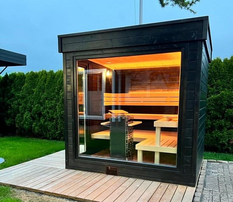 Un sauna en bois noir est installé en extérieur.