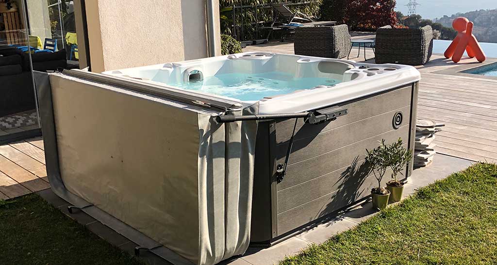 Spa H455 posé sur une terrasse en bois dans le jardin d'une maison