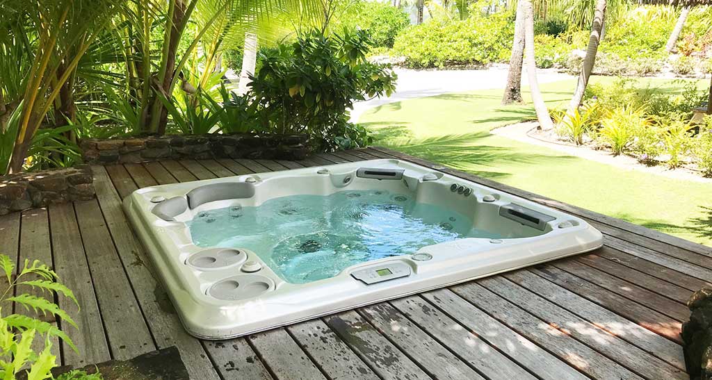 Spa encastrer sur une terrasse en bois dans un jardin avec beaucoup de verdure.