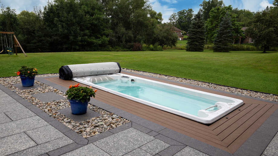 Un spa de nage, encastré dans une terrasse, est installé en extérieur et offre une vue sur un grand jardin. 