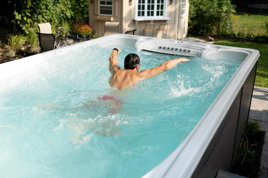 Un spa de nage hors sol est installé en extérieur. Un homme pratique la nage sportive grâce au système de nage à contre-courant. 