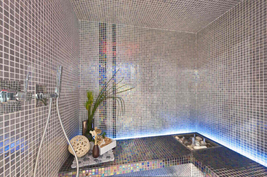 Intérieur d'un hammam au design contemporain, recouvert de mosaïque et équipé d'une douchette. 