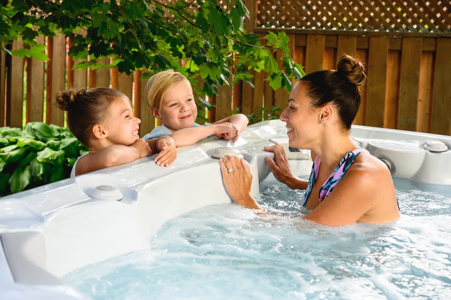 Une femme installée dans un spa hors sol discute avec ses enfants. 