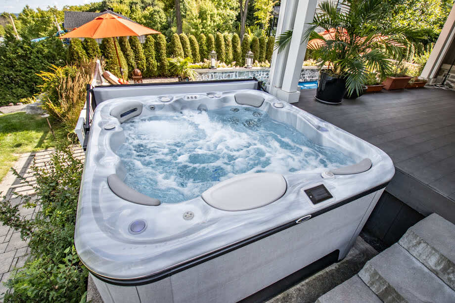 Un bain à remous hors sol est installé dans un jardin, à proximité de la terrasse et de la maison. 